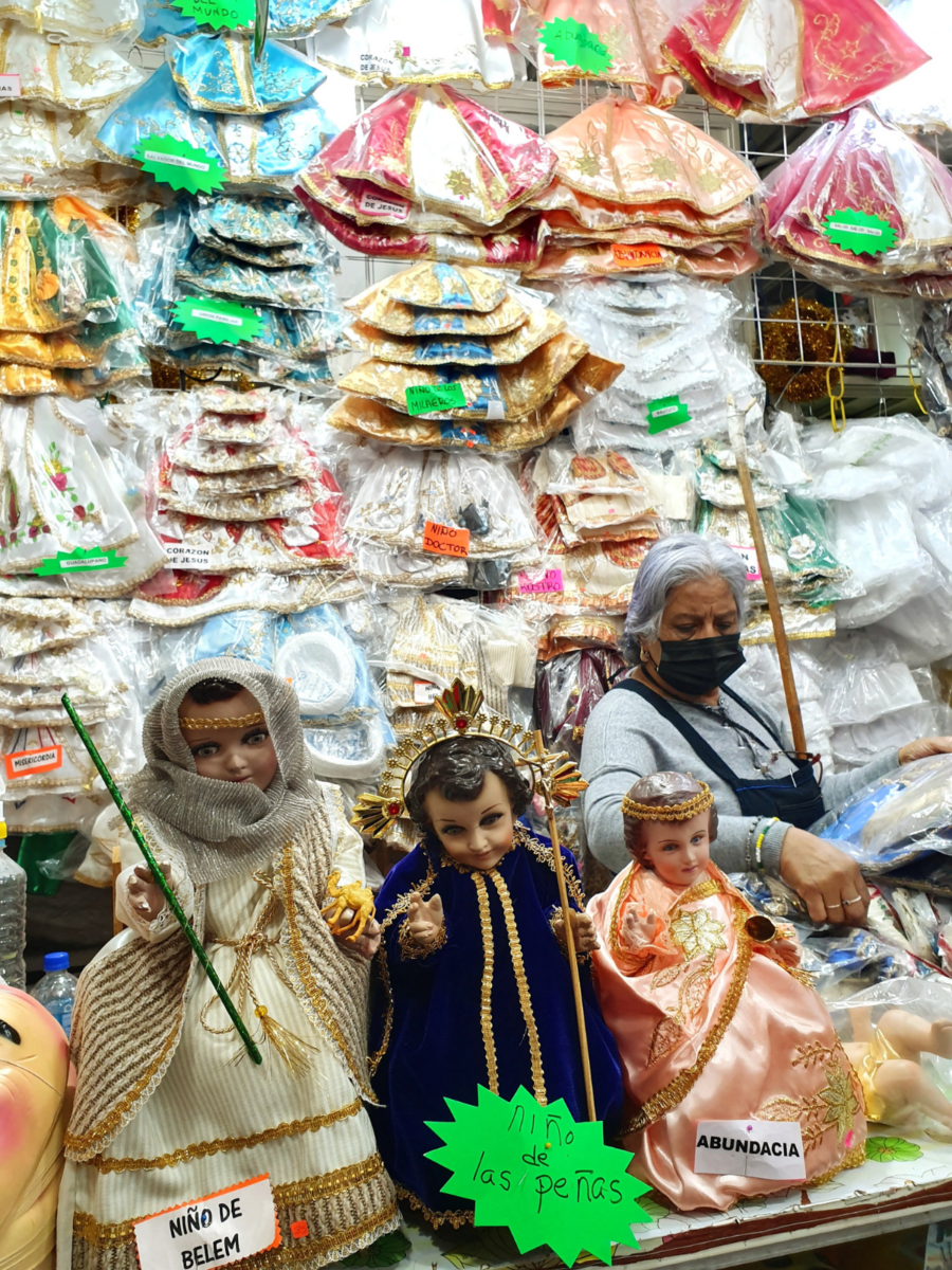 Verkoopster in haar marktkraam vol nieuwe kleertjes voor de Niños Dios in Oaxaca, Mexico