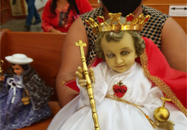 Mexicaanse gelovige toont trots haar Niño Dios of Jezuspop met witte jurk en kroontje